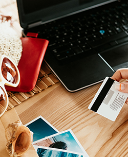 hand with credit card next to traveling items and laptop